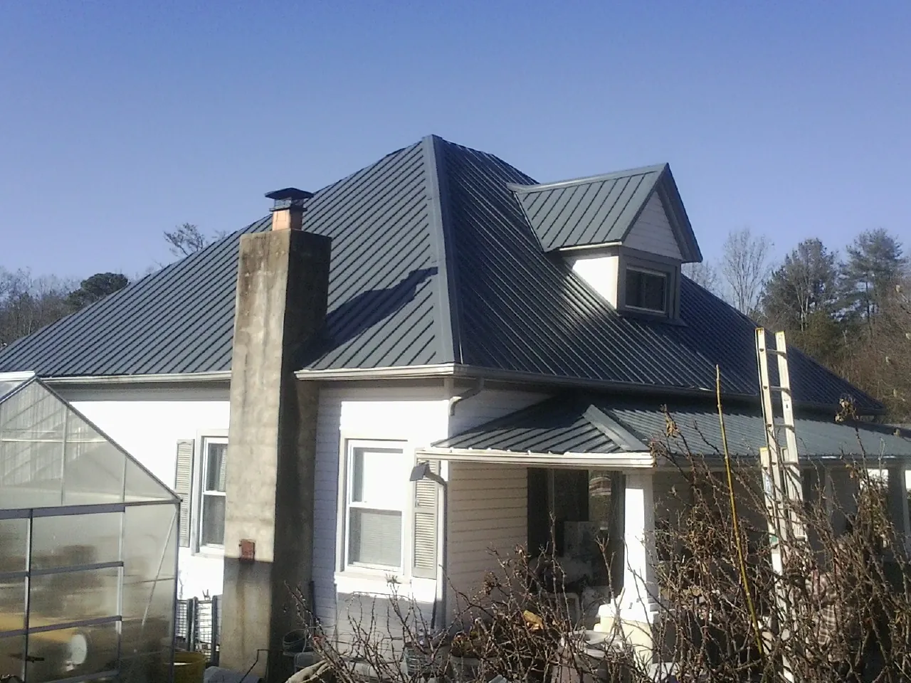 Dark blue standing seam metal roof on a white farmhouse with dormer — Slate & Tile Roof Repair by Roofing Brothers in Bella Vista