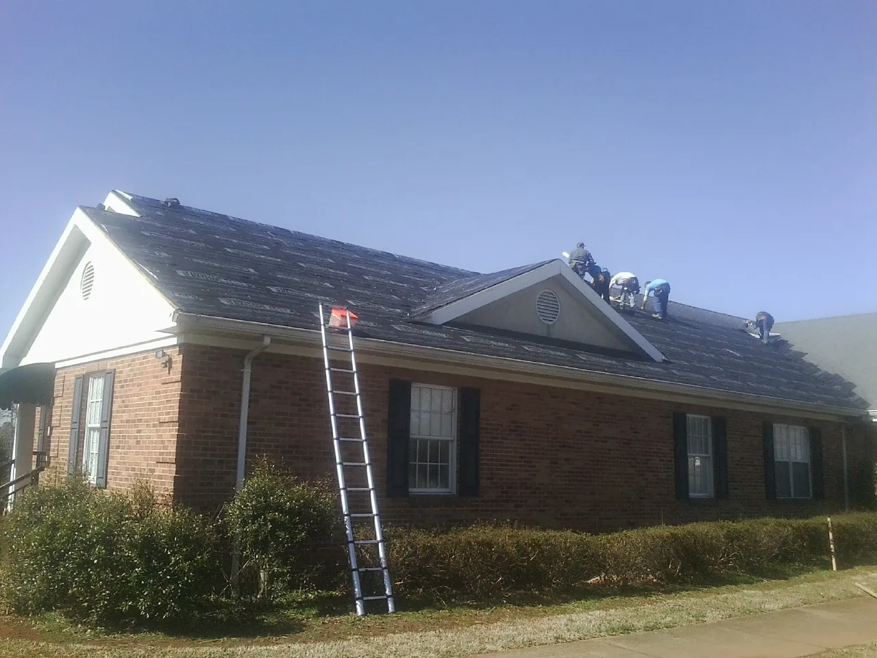 Crew tearing shingles off a brick ranch roof with a ladder set — Emergency Roof Repair work by our crew in Bella Vista