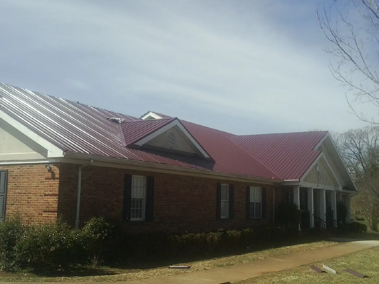 Red metal roof with gabled entries on a long brick building, from a Hail Damage Roof Repair job in Bella Vista