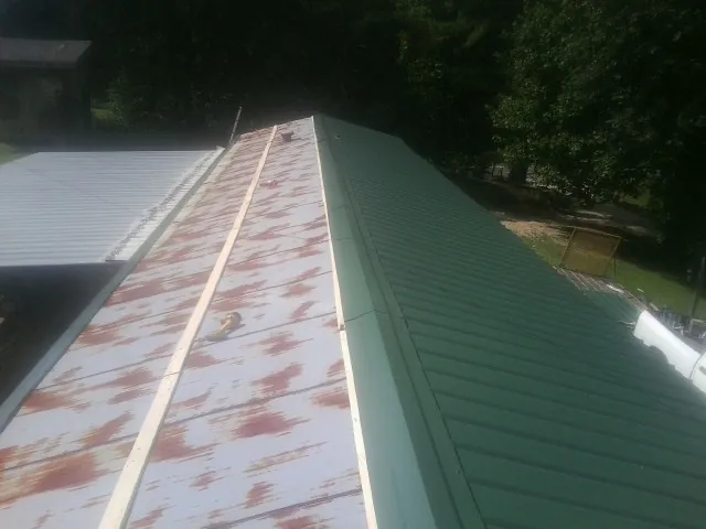 Old rusted panels beside newly installed green metal roofing — Wind Damage Roof Repair by Roofing Brothers in Bella Vista