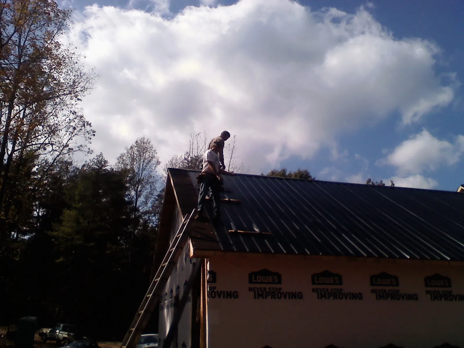 Roofer fastening dark metal panels high against a cloudy sky, from a Roof Inspection job in Bella Vista