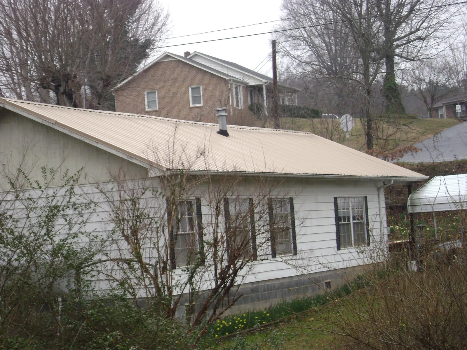 Tan metal roof on a white sided house set into a hillside — Commercial Roofing by Roofing Brothers in Bella Vista