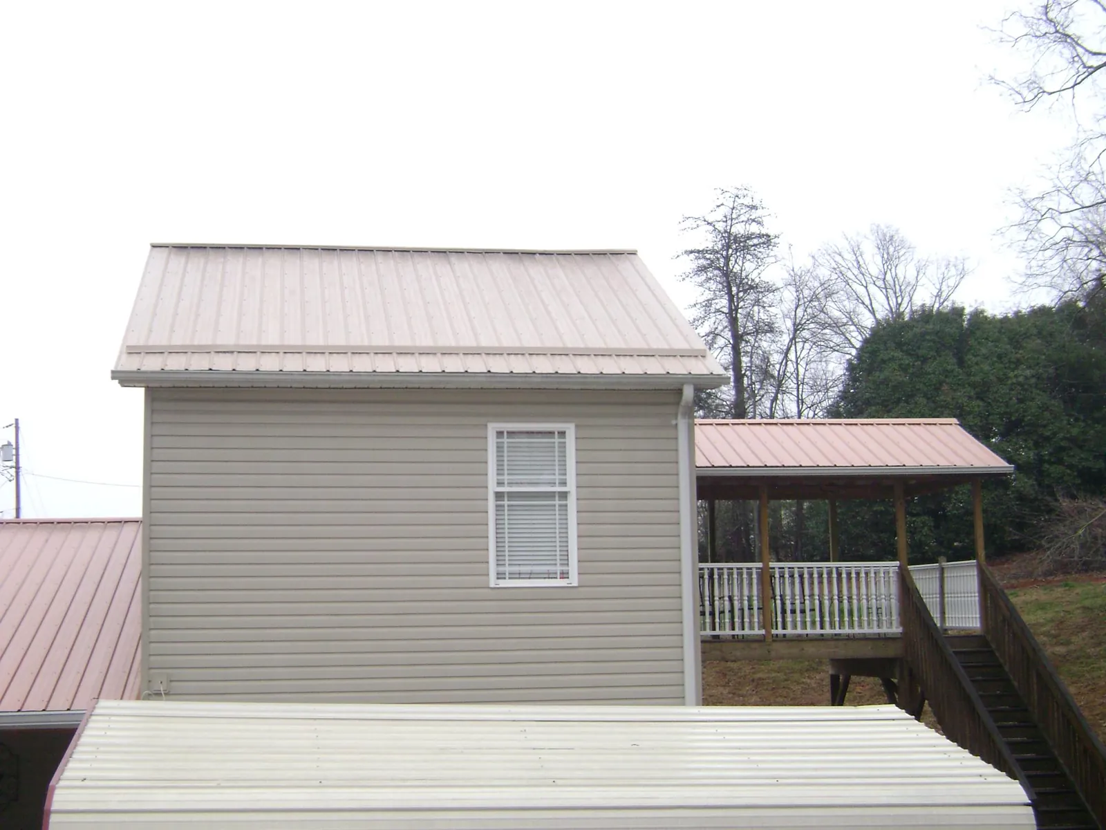Tan metal roofs on a two story addition and attached porch, from a Roof Replacement job in Bella Vista